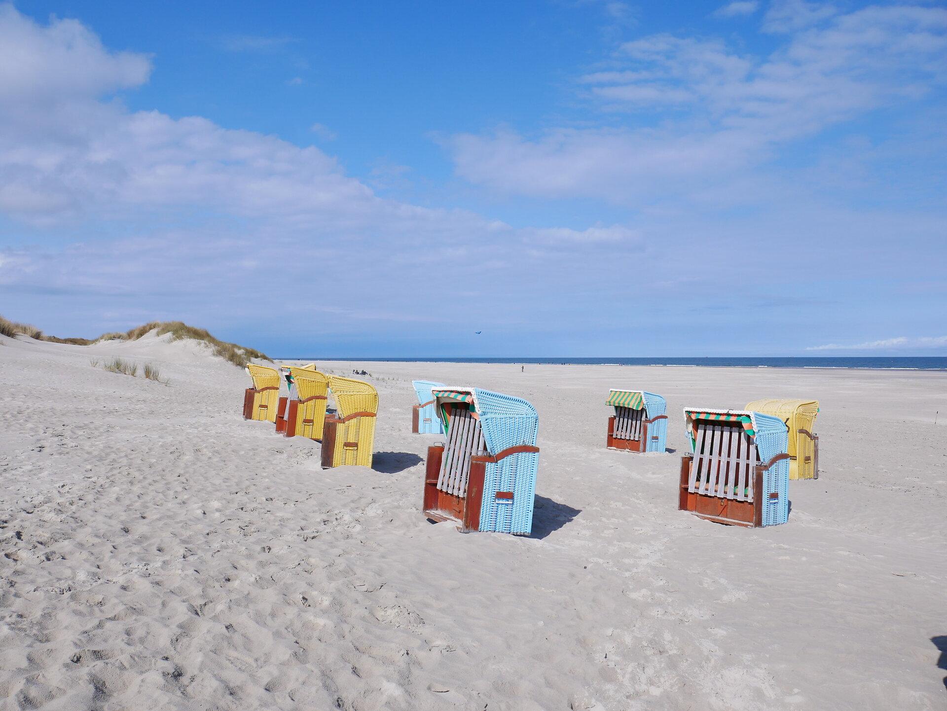 gelbe, weiße und blaue Strandkörbe am Strand von Juist mit Blick auf Dünengraslandschaft und Meer
