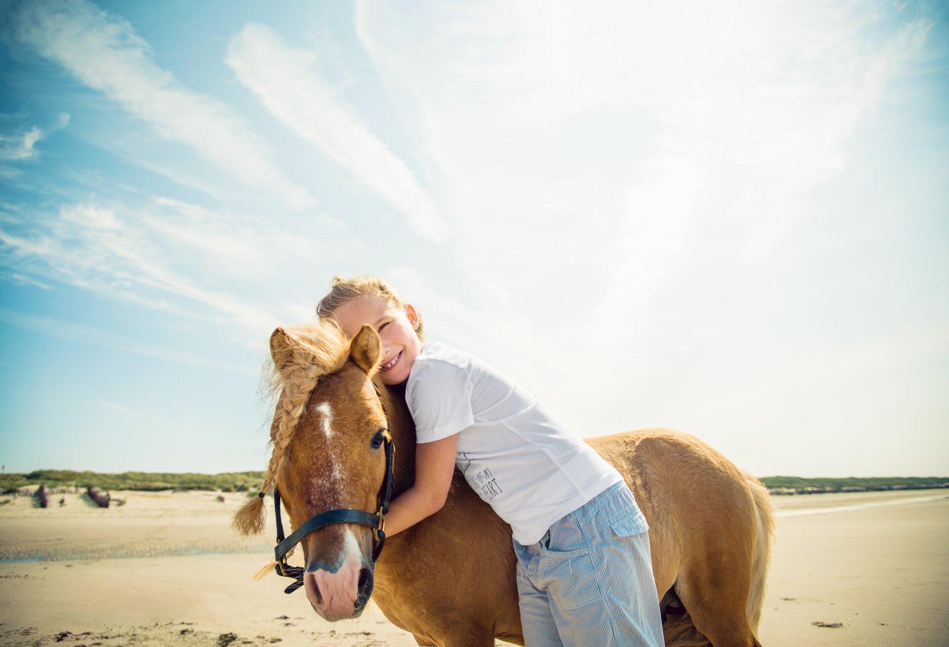 Kind umarmt Pony am Strand auf der Insel Juist