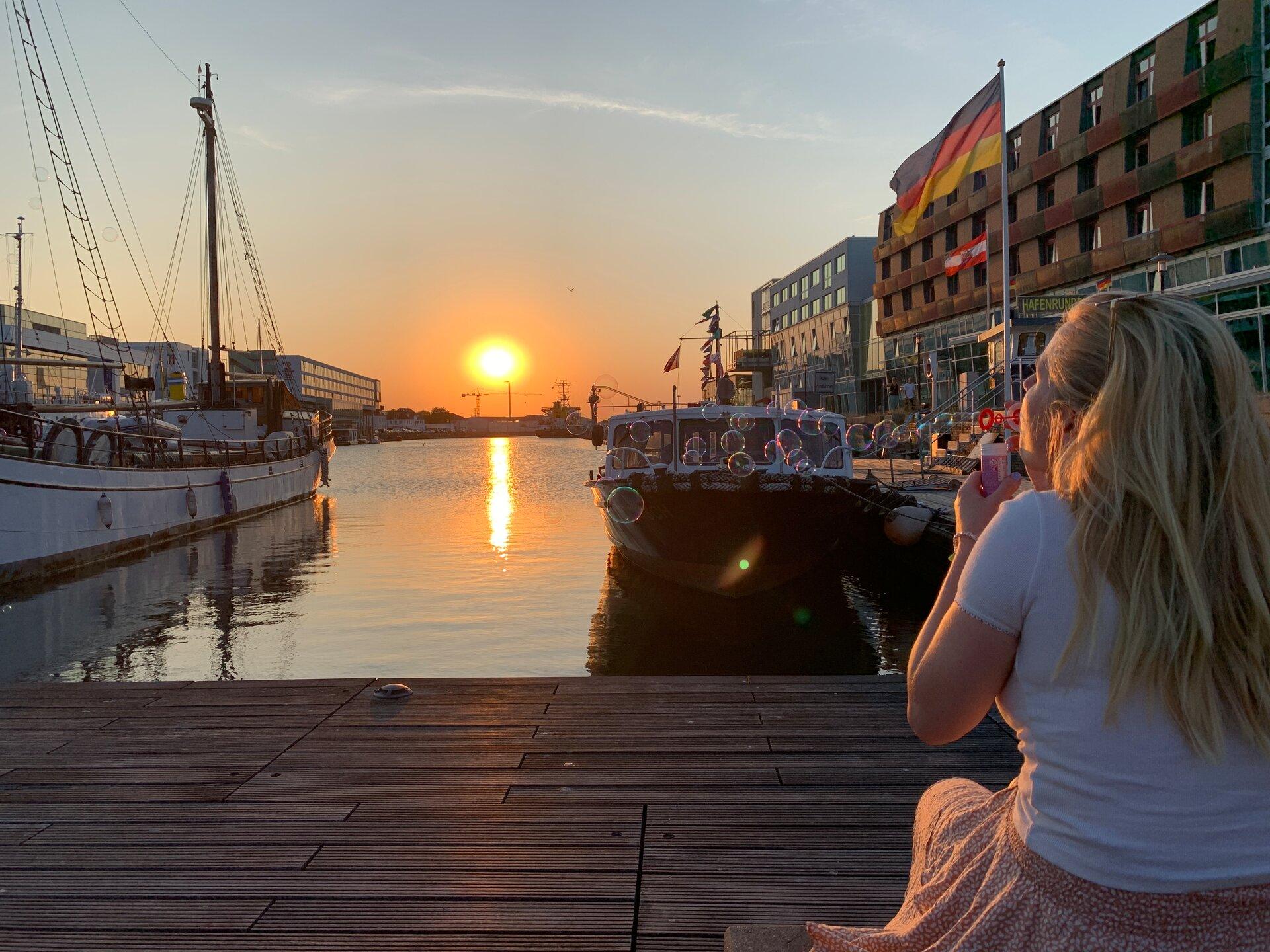 Frau pustet Seifenblasen am Hafenbecken bei Sonnenuntergang in Bremerhaven 