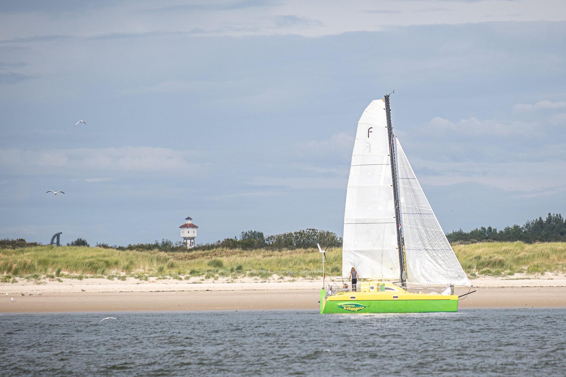 grünes Segelschiff vor der Insel Langeoog mit Blick auf den Wasserturm