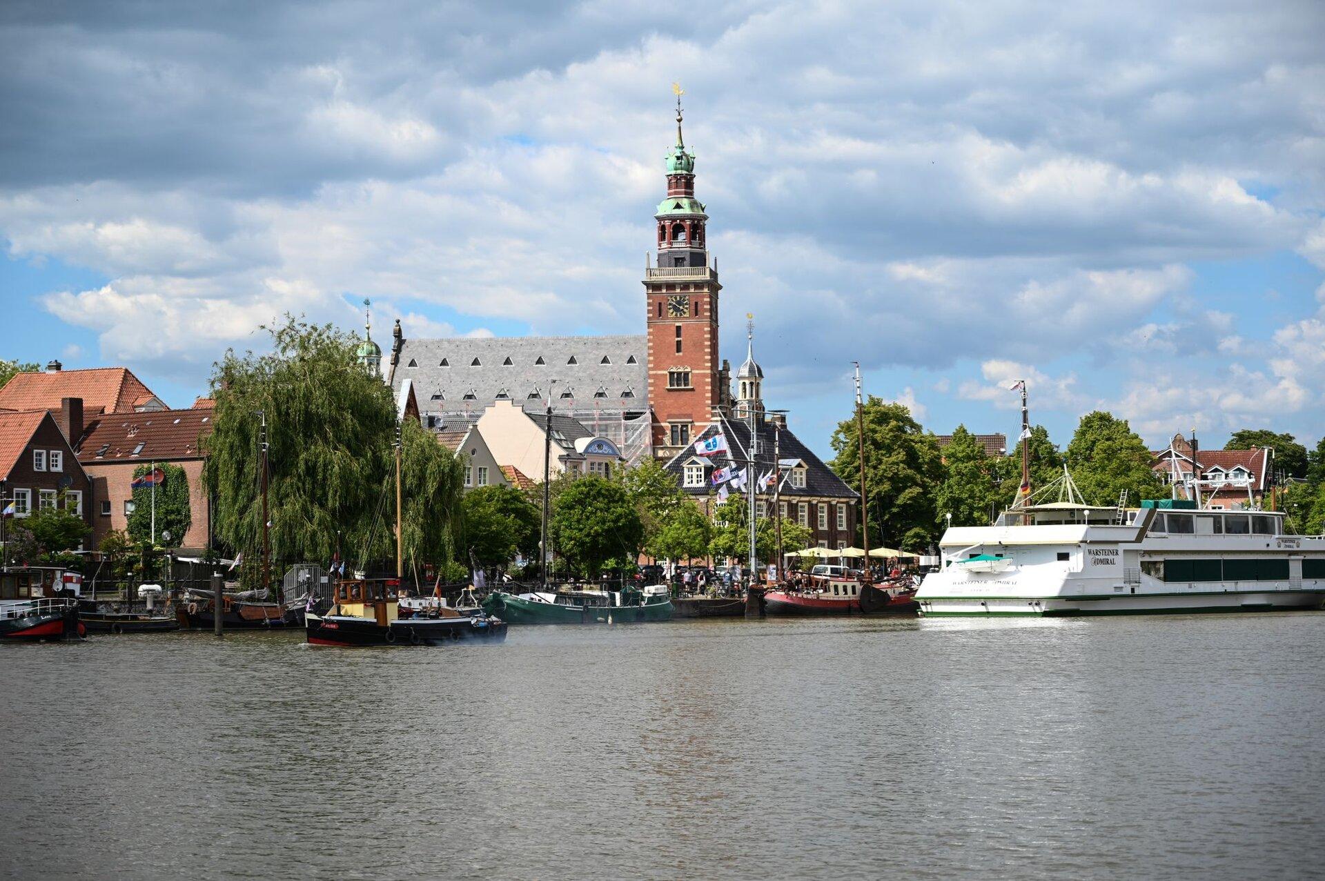 Blick auf die Uferpromenade mit Booten in Hafenbereich und dem Rathaus im Hintergrund in Leer